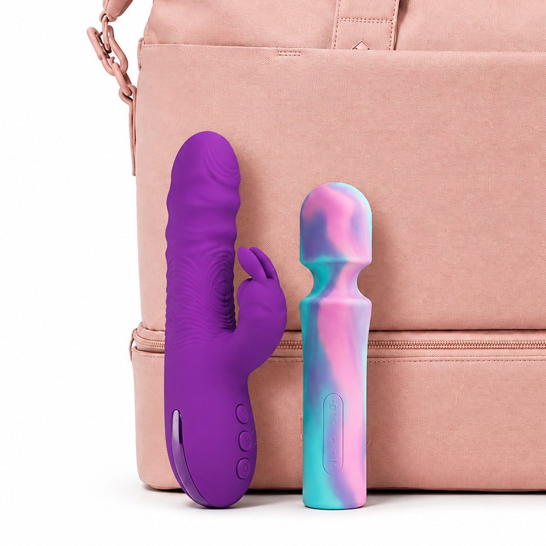 Two personal massagers standing in front of a blush pink bag on a white studio background. One is solid purple with a textured ribbed surface, and the other has a pastel marbled pattern in pink, blue, and teal.